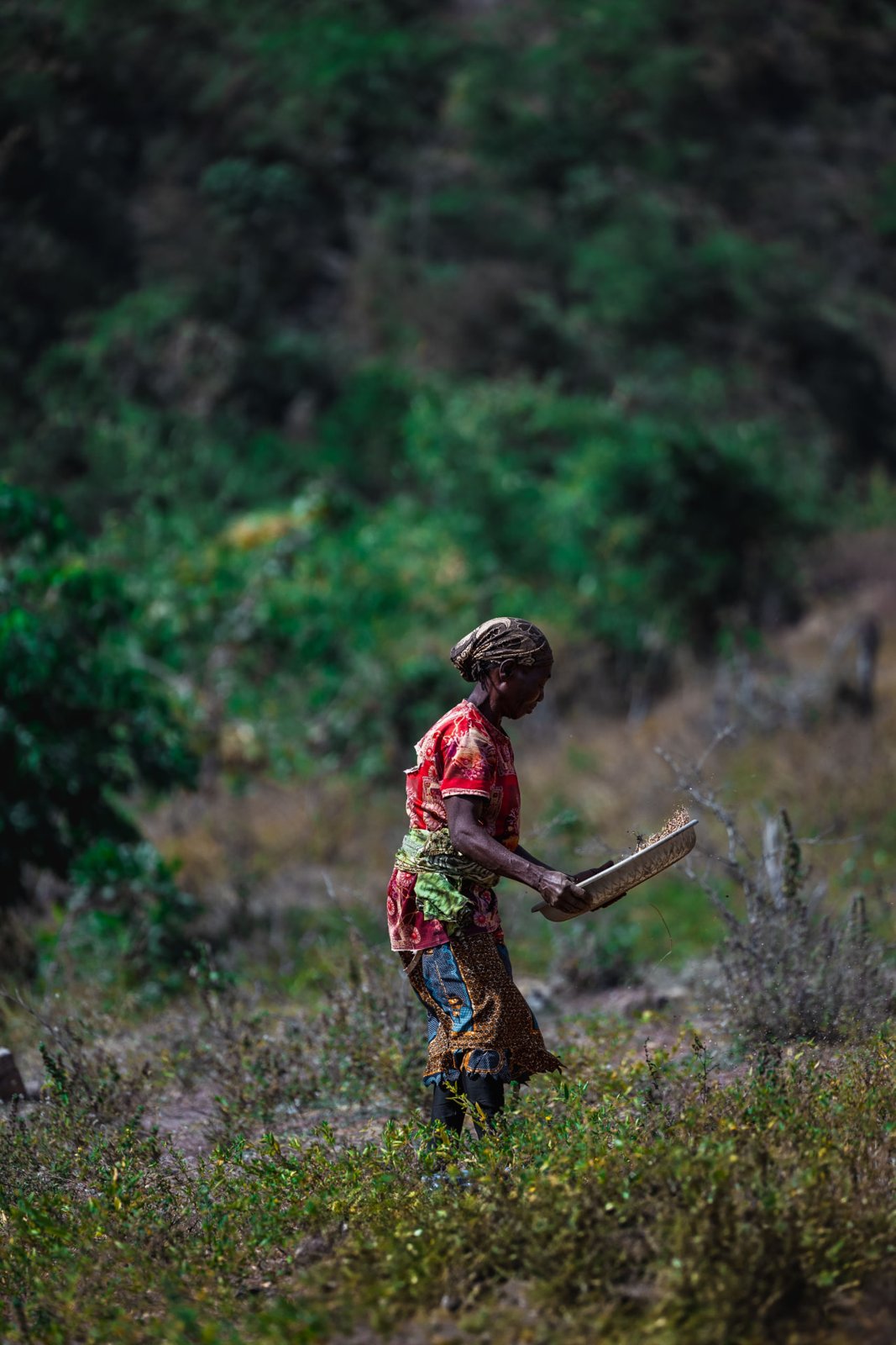Femme avec un outil agricole dans une parcelle entourée de végétation.
